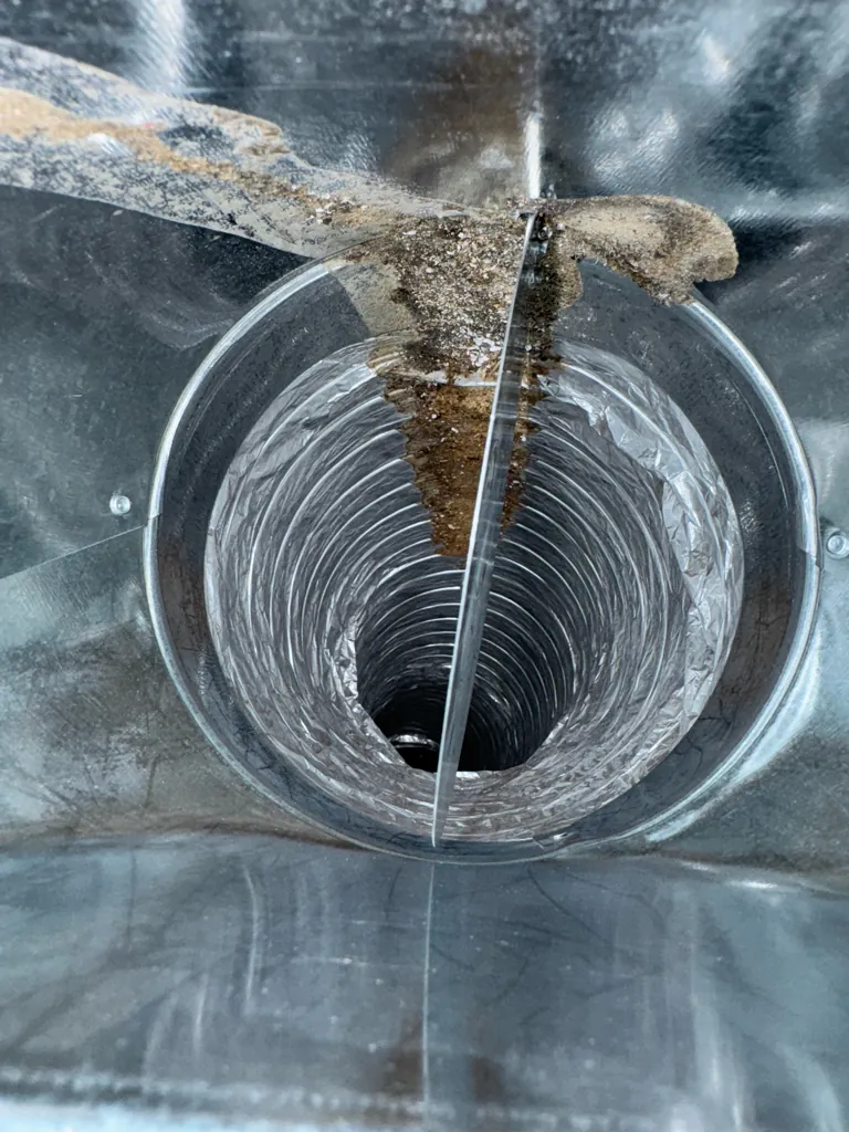Duct takeoff with a trail of construction debris spilling over the collar, before cleaning
